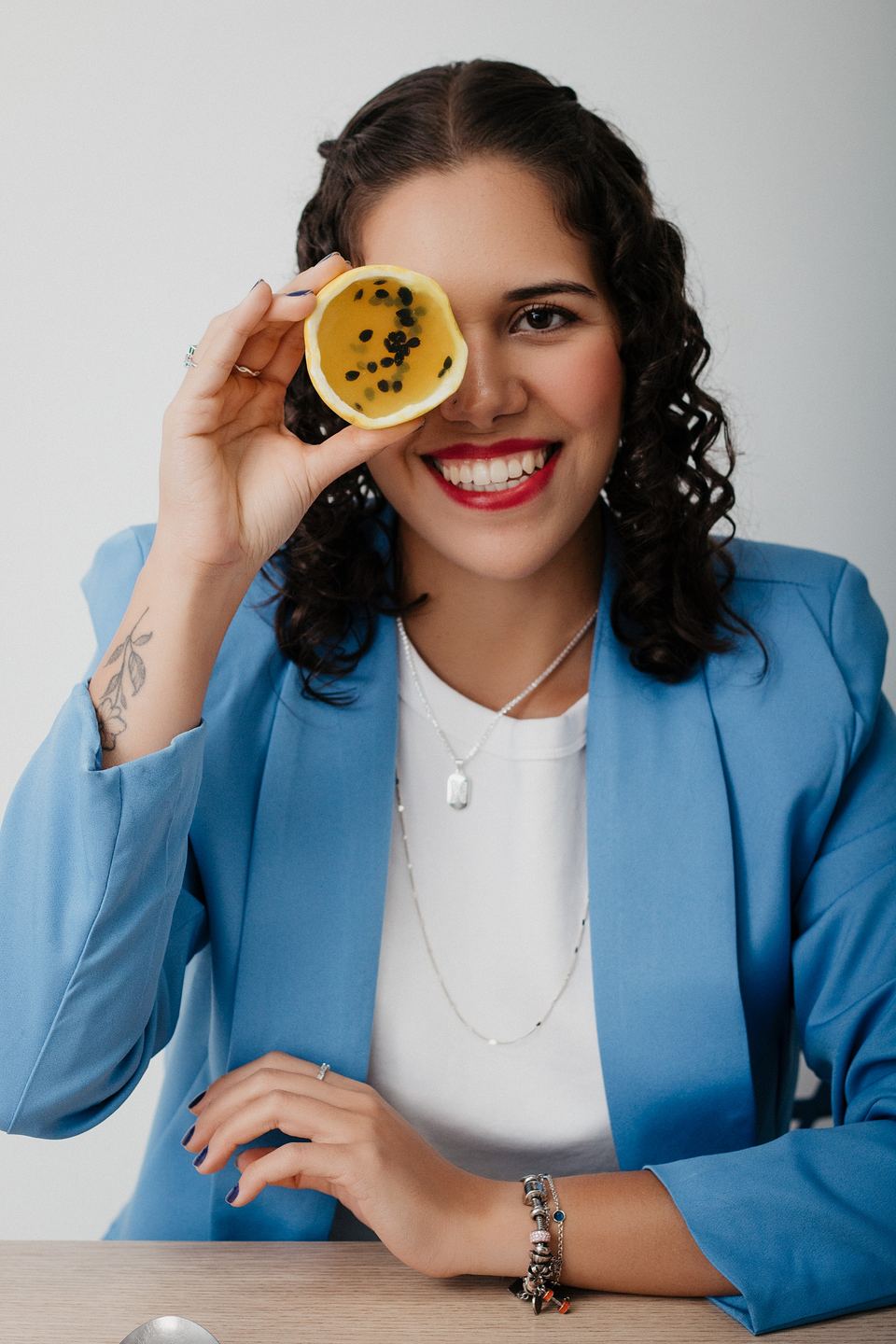 Nicoli Nascimento sorrindo, segurando meio maracujá na frente de um dos olhos